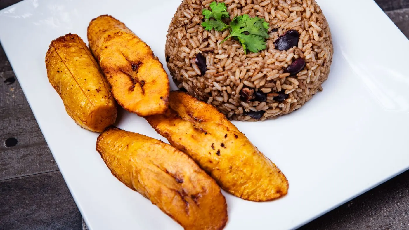 Plato blanco con una porción de arroz con fríjoles y cuatro tajadas de plátano frito, una comida con carbohidratos complejos de la cocina colombiana