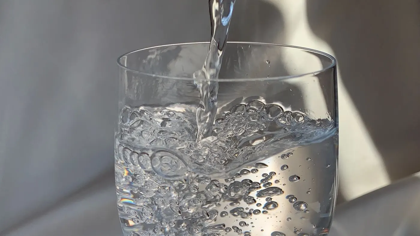 Vaso de vidrio al que cae un chorro de agua en primer plano, el líquido con el que se toma el psyllium