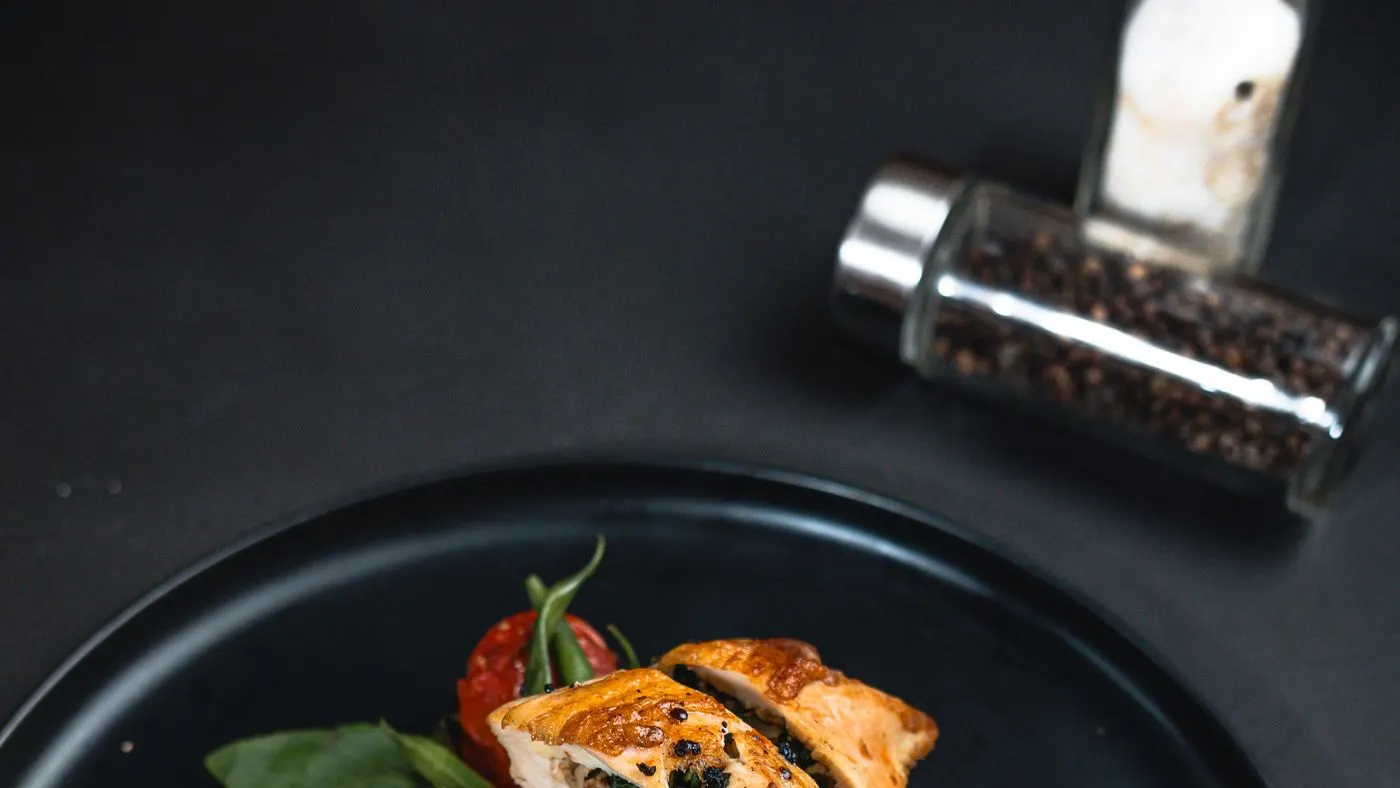 Plato blanco con trozos de pollo en salsa, habichuelas verdes y cebolla larga picada, con tenedor y cuchillo al lado